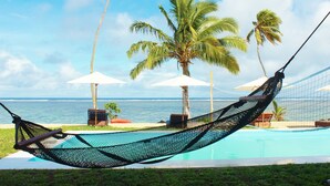 A hammock by a pool with palm trees and umbrellas in the background. - Coral Lagoon Fiji Resort (Korolevu)