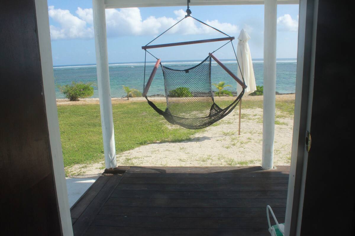Uitzicht vanaf een overdekt terras op een strand met een hangmat.