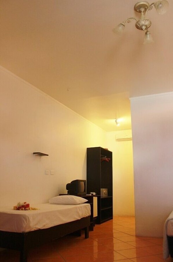 A small, simple room with a single bed, a television, and a black shelving unit.