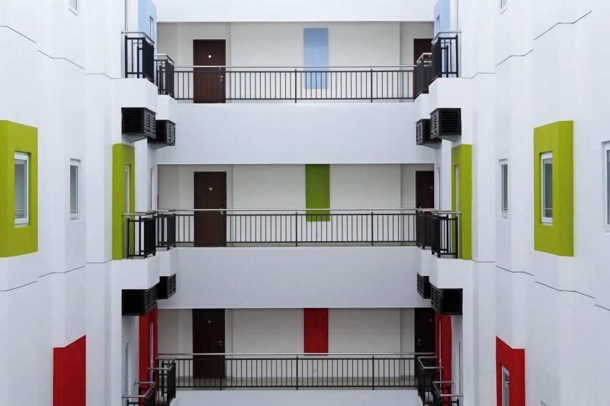 Un immeuble à plusieurs étages doté d’une cour intérieure, avec des balcons pourvus de garde-corps et des portes à chaque étage.