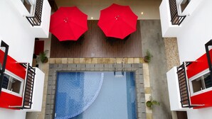 Ein Poolbereich auf dem Dach mit zwei roten Sonnenschirmen, einer Glasbrüstung und Kübelpflanzen.
