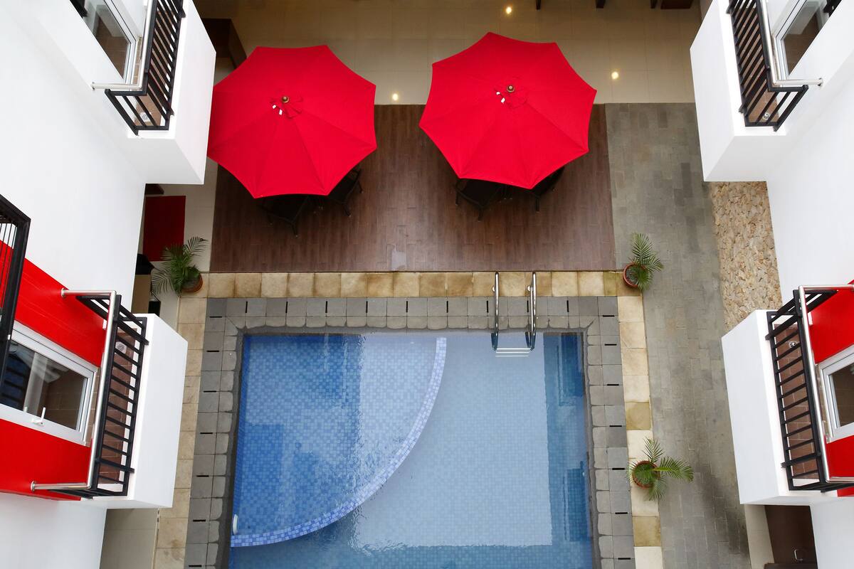 Zona de piscina en la azotea con dos sombrillas rojas, barandilla de cristal y plantas en macetas.