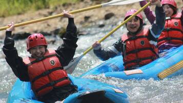 Un grupo de personas en una balsa inflable azul, cada uno con chaleco salvavidas rojo y casco, remando por un río.