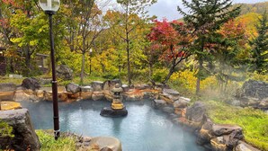A hot spring surrounded by rocks and autumn foliage. - Niseko Grand Hotel (Niseko)