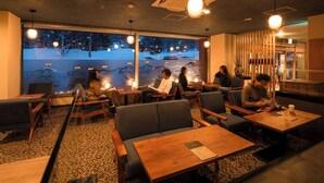 A restaurant with wooden tables and chairs, a patterned carpet, and a large window with a view of snow-covered trees. - Niseko Grand Hotel (Niseko)