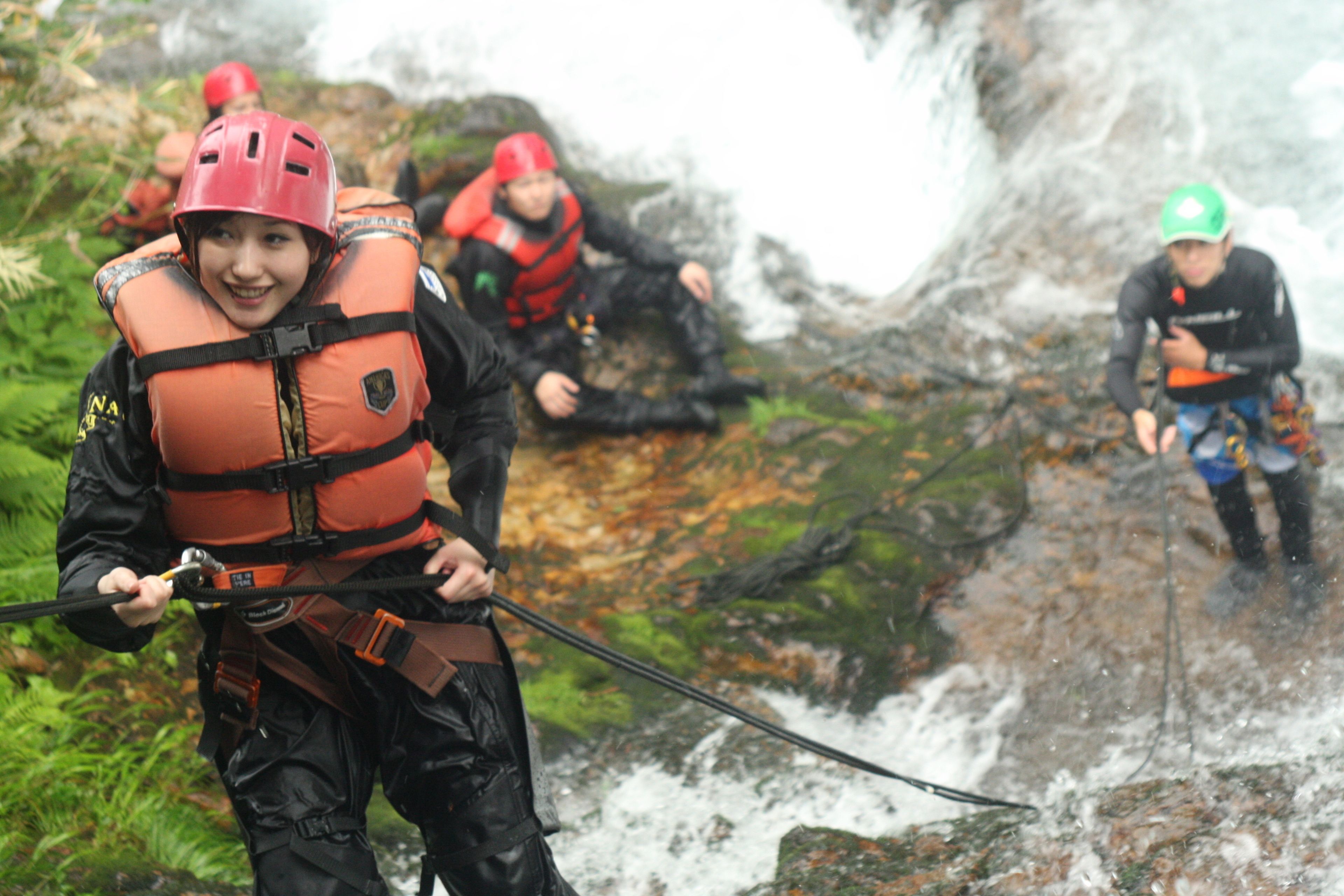 A group of people in outdoor gear, including life jackets and helmets, near a waterfall.