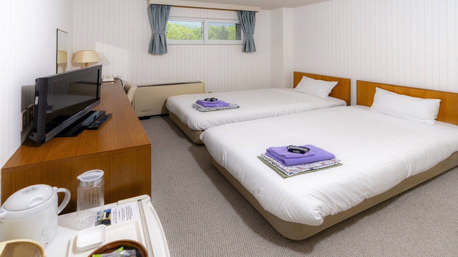 A hotel room with two beds, a desk with a TV, a coffee maker, and a window with curtains.