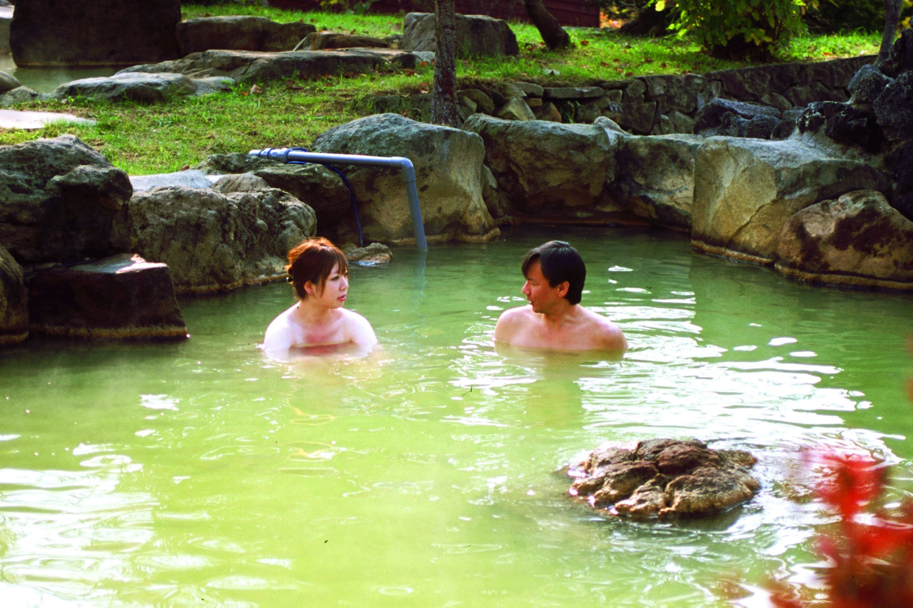 A natural hot spring with large rocks and a wooden walkway.