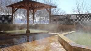 A hot spring area with a wooden gazebo, tiled flooring, and a fenced enclosure. - Niseko Grand Hotel (Niseko)