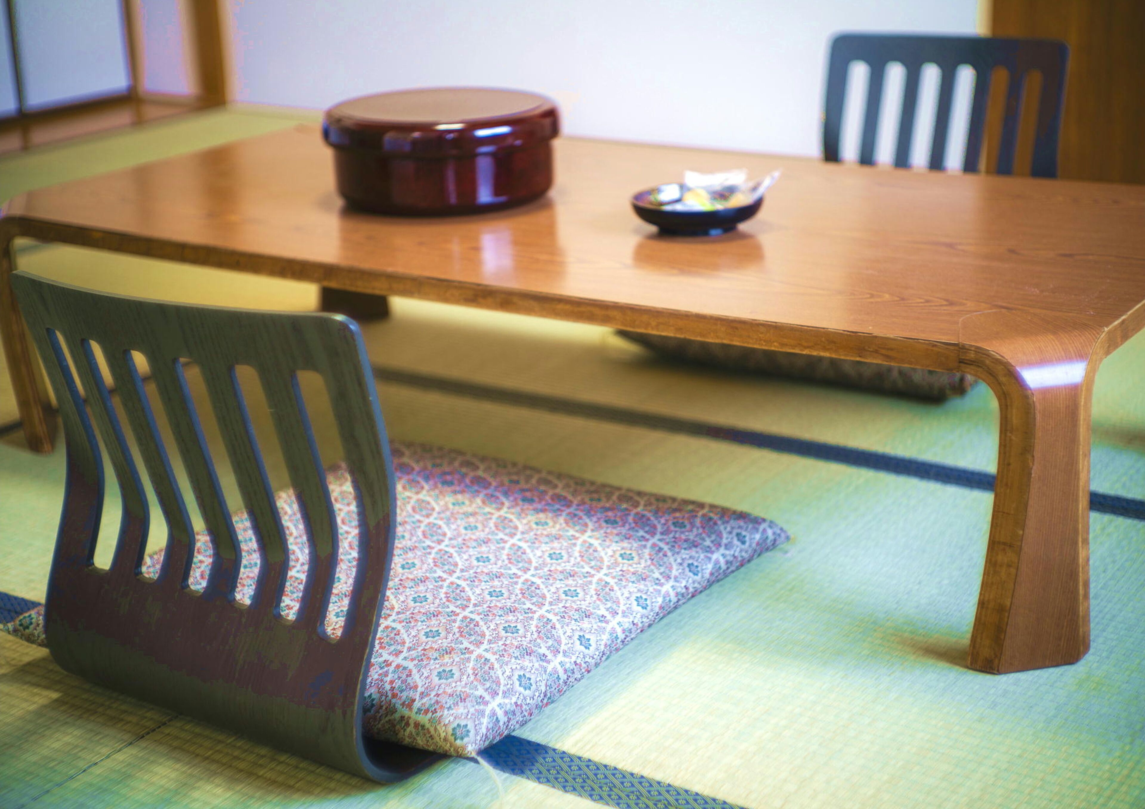 A wooden dining table with a patterned cushion and a small bowl on it.