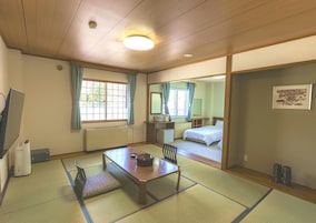 A traditional Japanese-style room with tatami flooring, a low table, a bed, a desk, and a window with curtains.
