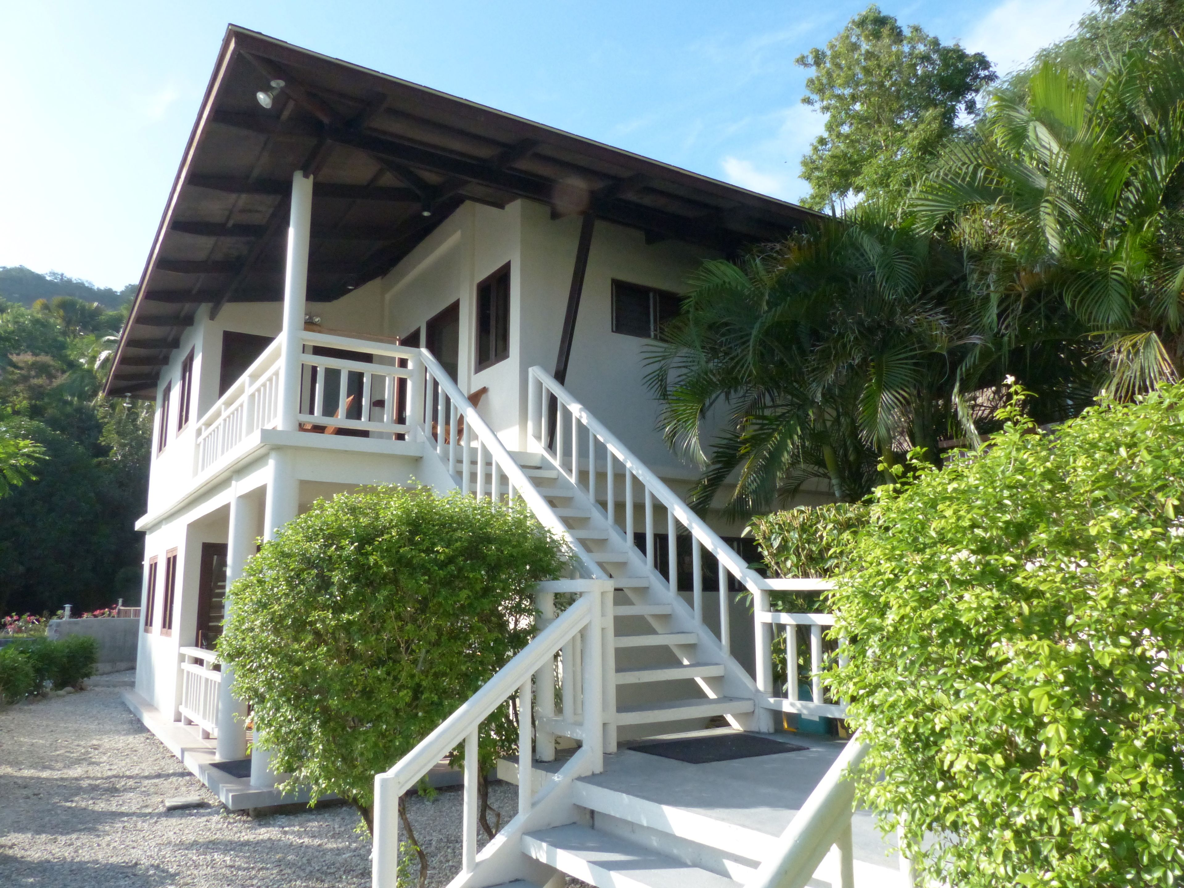 A two-story building with a white exterior, a balcony on the upper floor, and a staircase leading to the entrance.