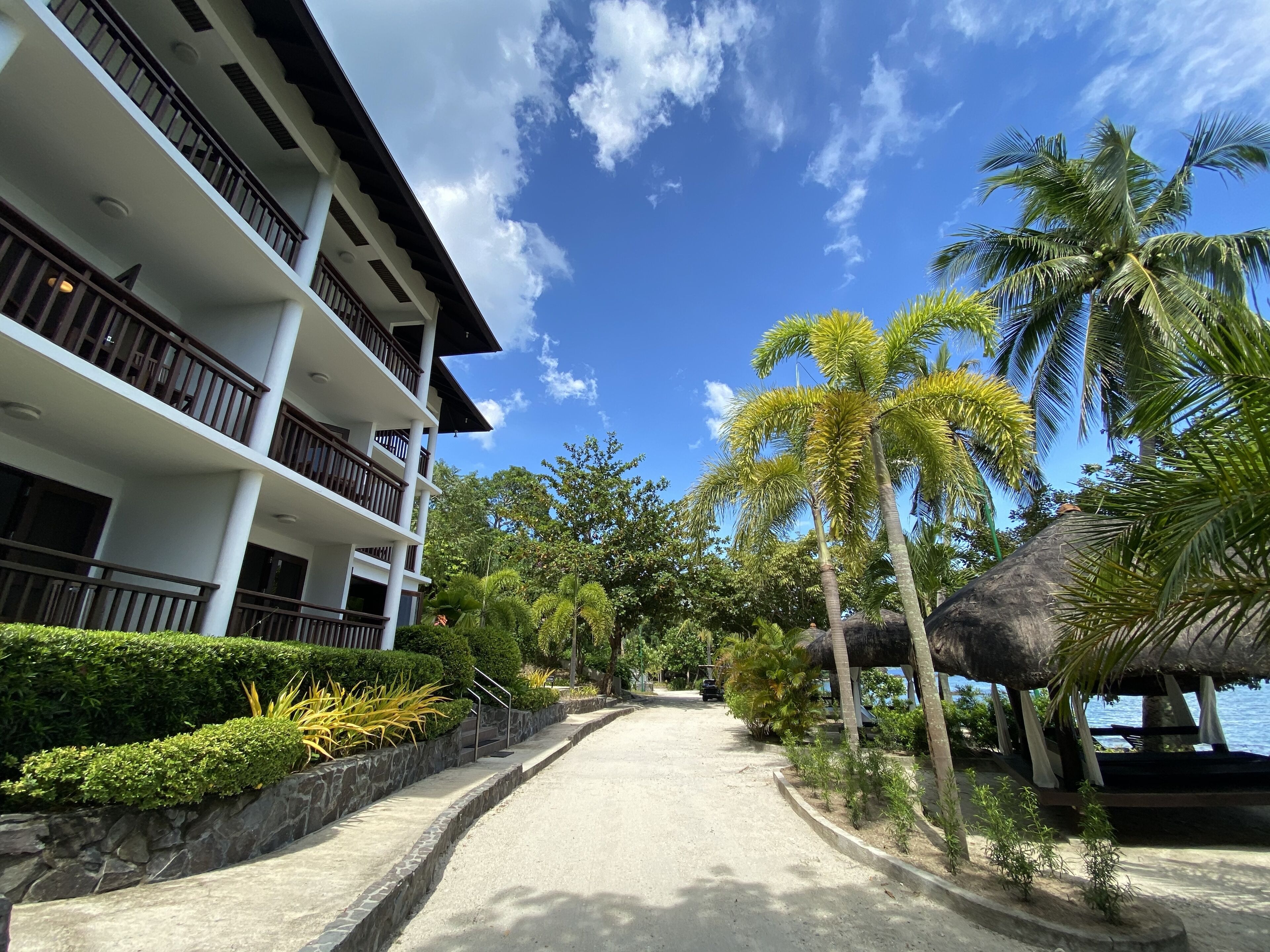 A resort with a multi-story building, a paved pathway, and palm trees.