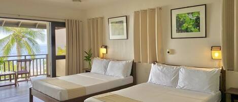 Habitación de hotel con dos camas, un balcón con vistas a palmeras y una pequeña mesa.
