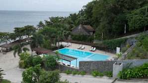 Zona de piscina con vista al mar, rodeada de vegetación exuberante y un muro de piedra.