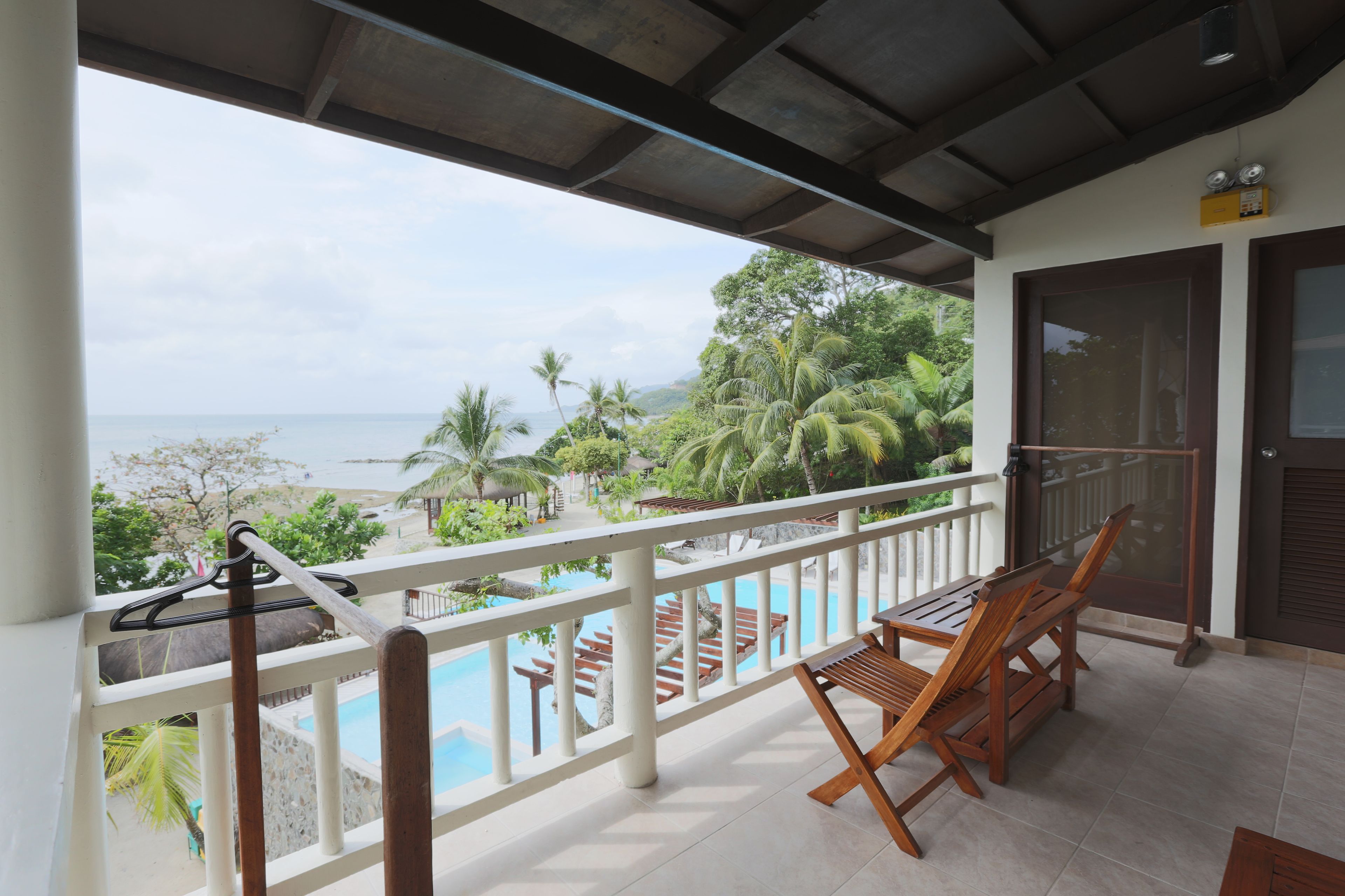 A balcony with a view of the ocean, wooden chairs, and a pool.