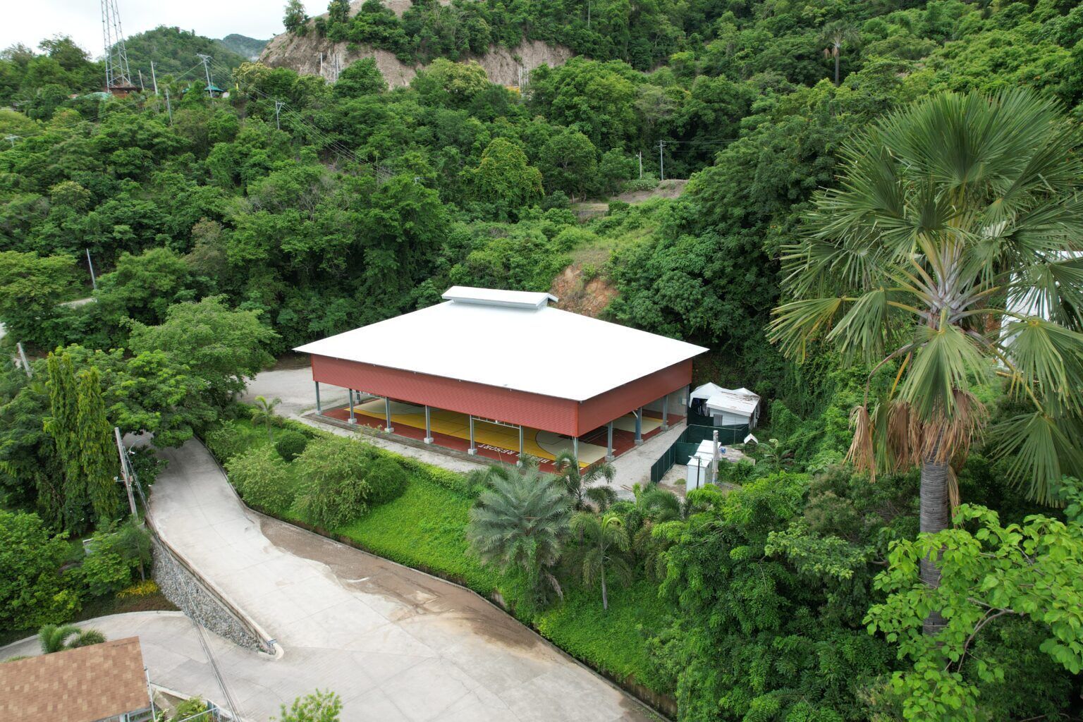 Um edifício rodeado por vegetação densa, com telhado plano e área externa coberta.