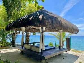 A beachside gazebo with a thatched roof, wooden benches, and a view of the ocean. - Palm Beach Resort (San Juan)