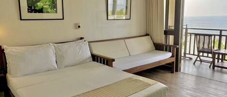 A hotel room with a bed, a sofa, a balcony with a view of the sea, and two framed pictures on the wall.