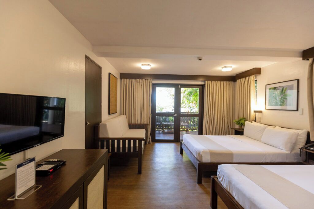 Habitación de hotel con televisión, dos camas, escritorio y balcón con cortinas.
