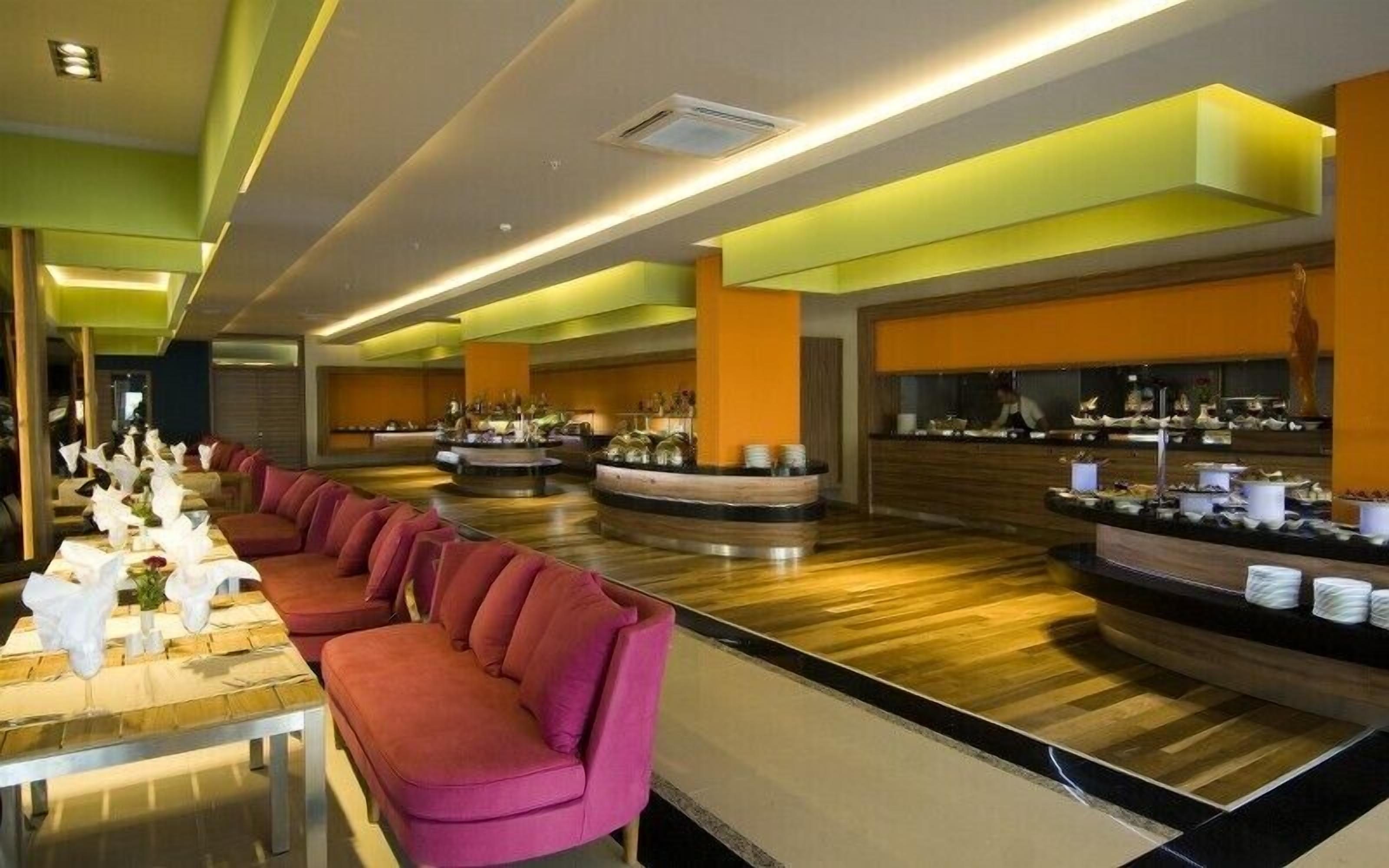 A modern hotel lobby with a long red sofa, a central round bar area, and a buffet setup.