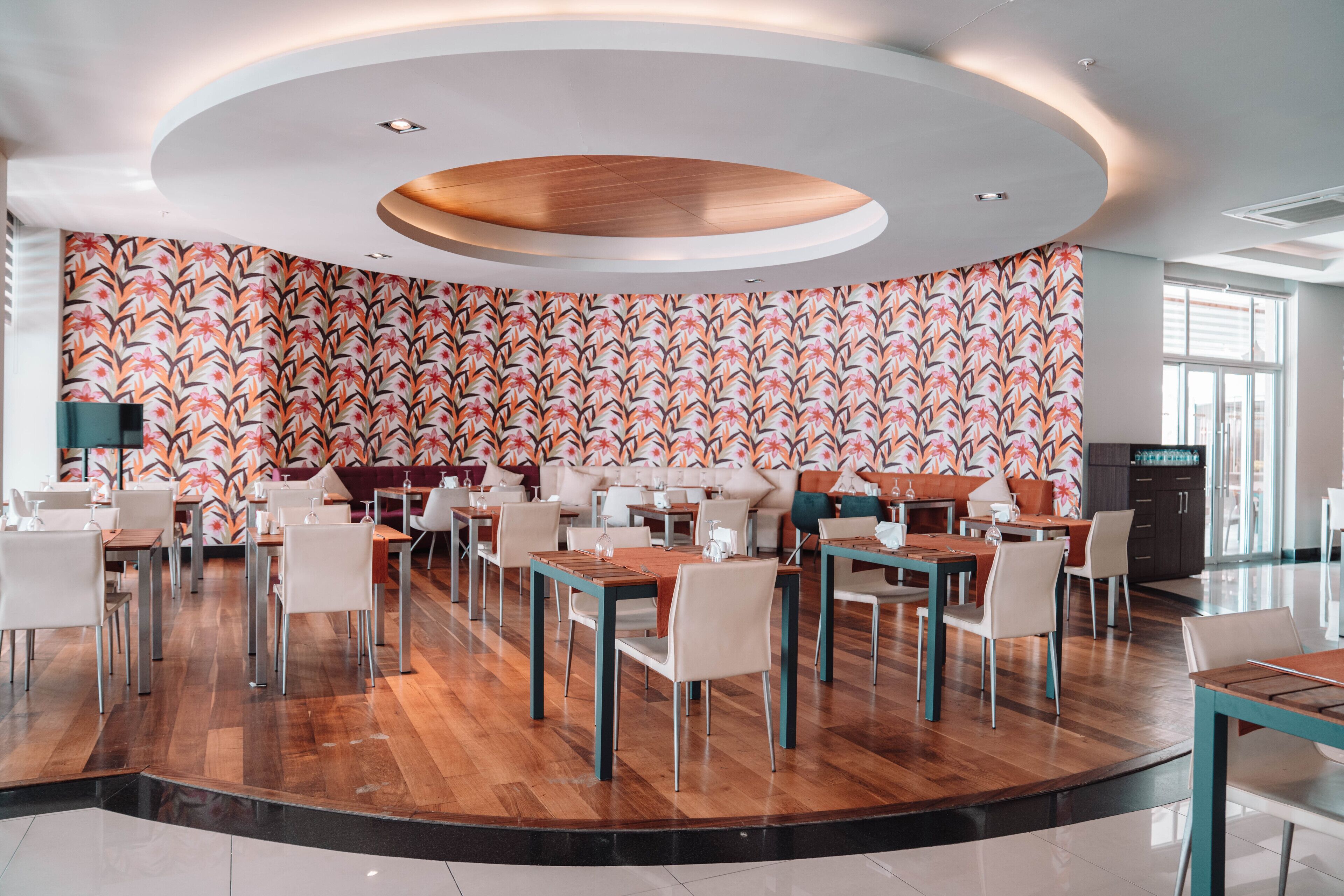 A modern restaurant with a circular seating area, wooden tables, and a patterned wall.