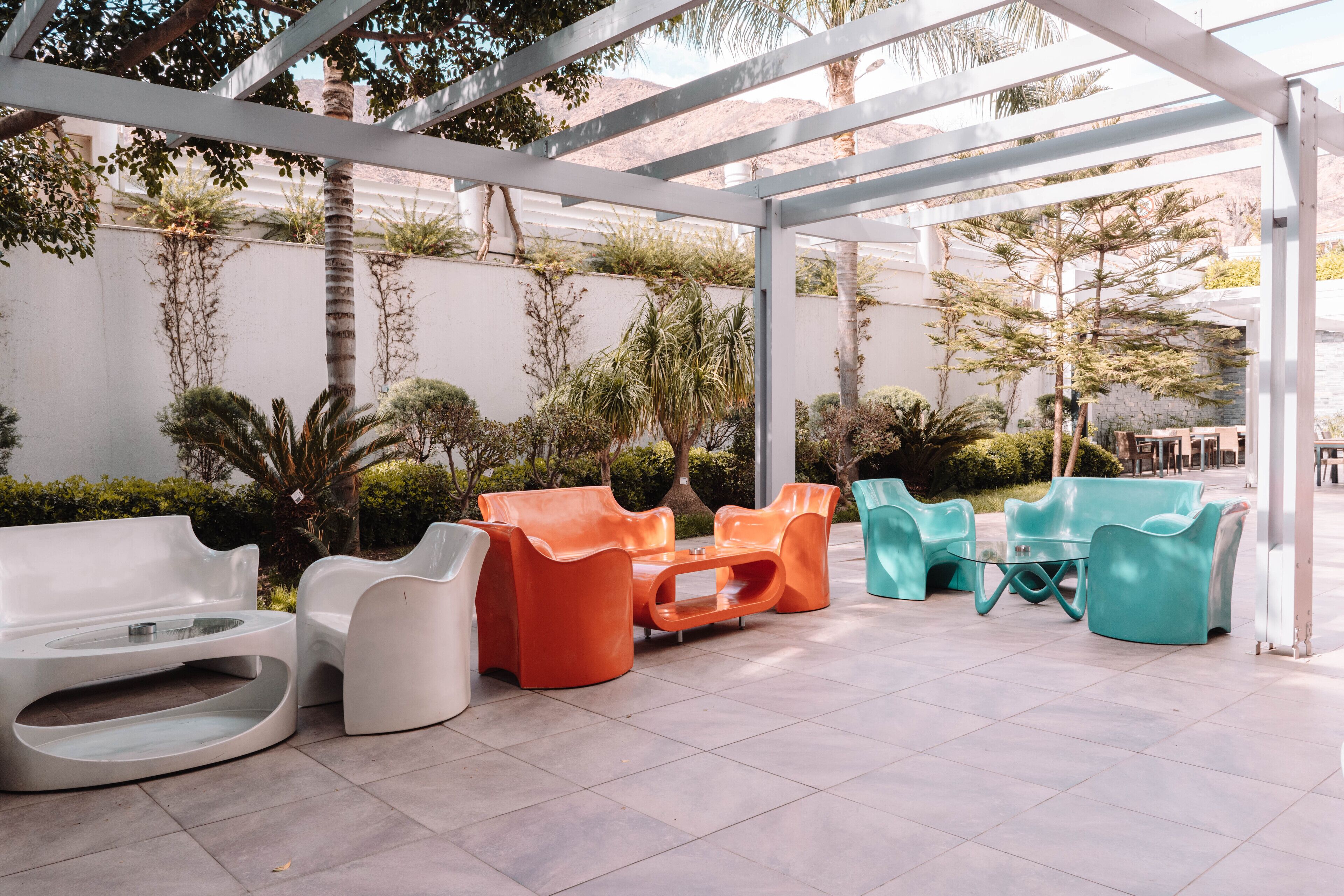 A covered outdoor seating area with modern, colorful chairs and a white bench.