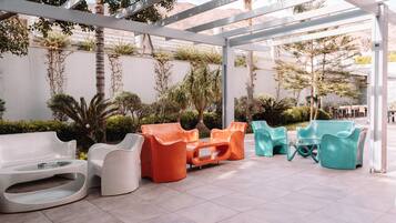 A covered outdoor seating area with modern, colorful chairs and a white bench.