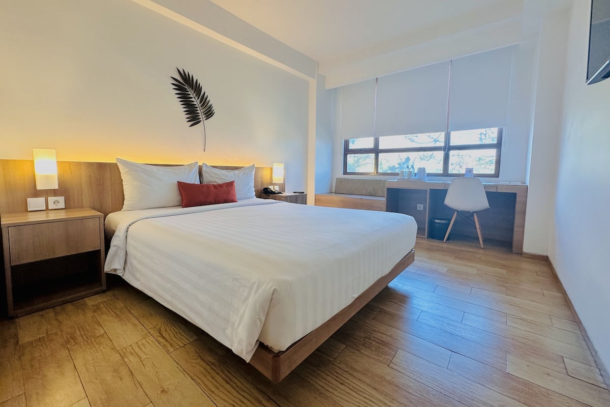 Moderni hotellihuone, jossa on suuri sänky, yöpöytävalaisimet, työpöytä ja ikkuna, josta on näkymä.