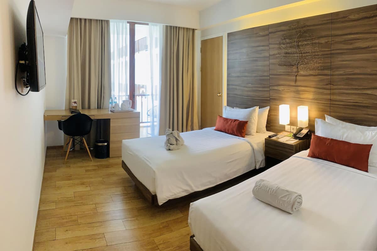 Hotellihuone, jossa on kaksi sänkyä, työpöytä, tuoli, televisio ja näkymä ulos.