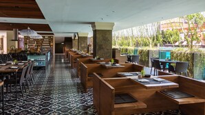 A restaurant with wooden booths, black and white patterned flooring, and a view of greenery and buildings outside. - Grand Zuri Kuta Bali (Kuta)