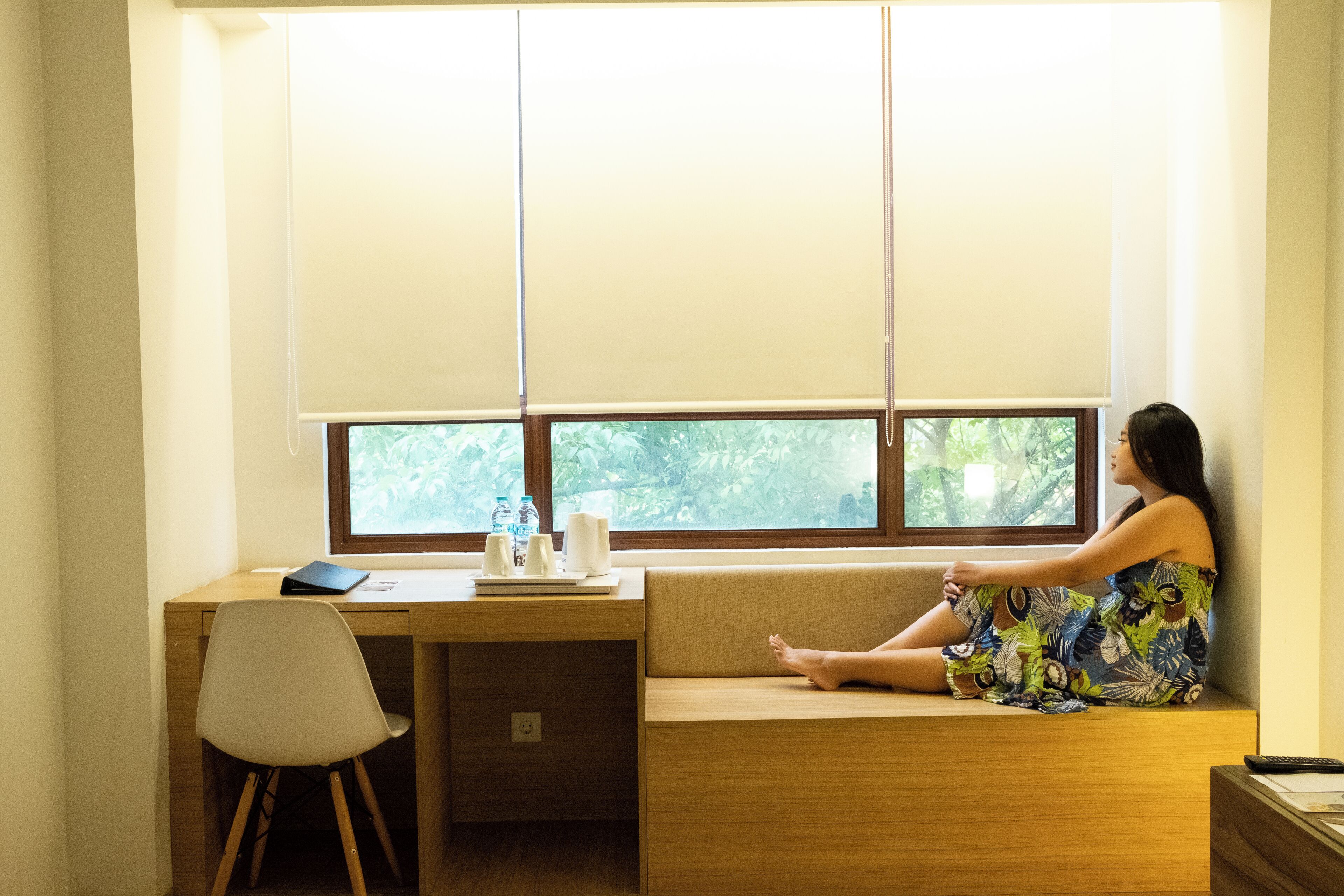 A room with a wooden desk, a cushioned bench, and a window with blinds.