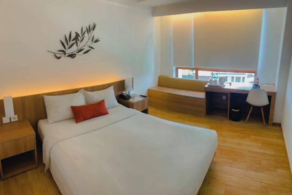 A modern hotel room with a large bed, a desk, and a window with a view.