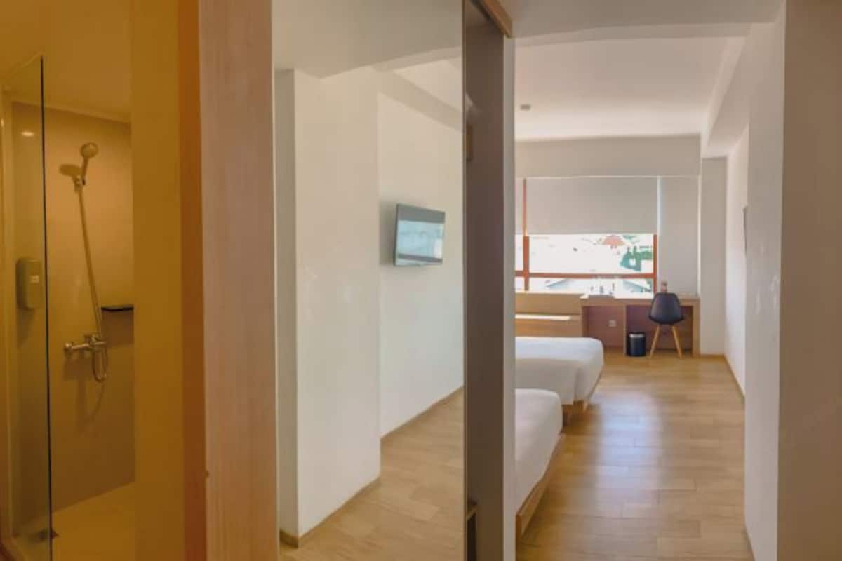 A hotel room with a shower, a bed, a desk, and a window.