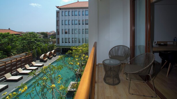 A balcony with a pool, lounge chairs, and a dining area with chairs and a table. - Grand Zuri Kuta Bali (Kuta)