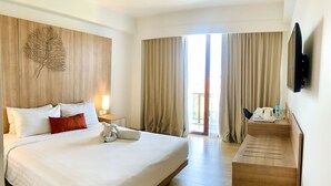 A hotel room with a large bed, a wooden desk, a flat-screen TV, and a balcony with curtains. - Grand Zuri Kuta Bali (Kuta)
