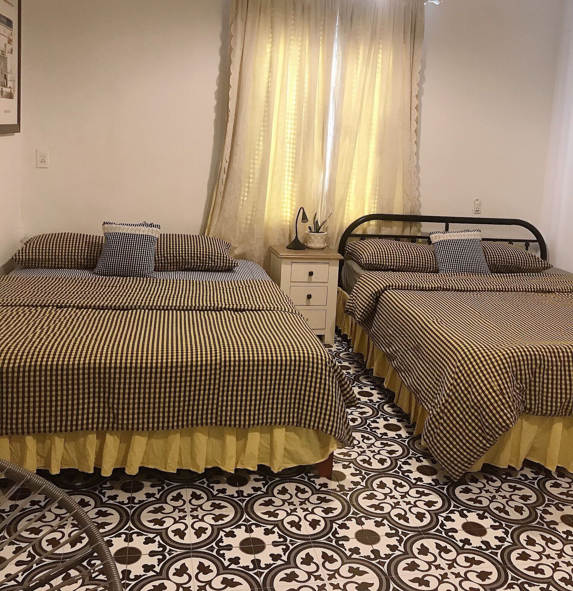 Una camera da letto con due letti, entrambi con lenzuola a quadretti, un comodino con una lampada e piastrelle a motivi.