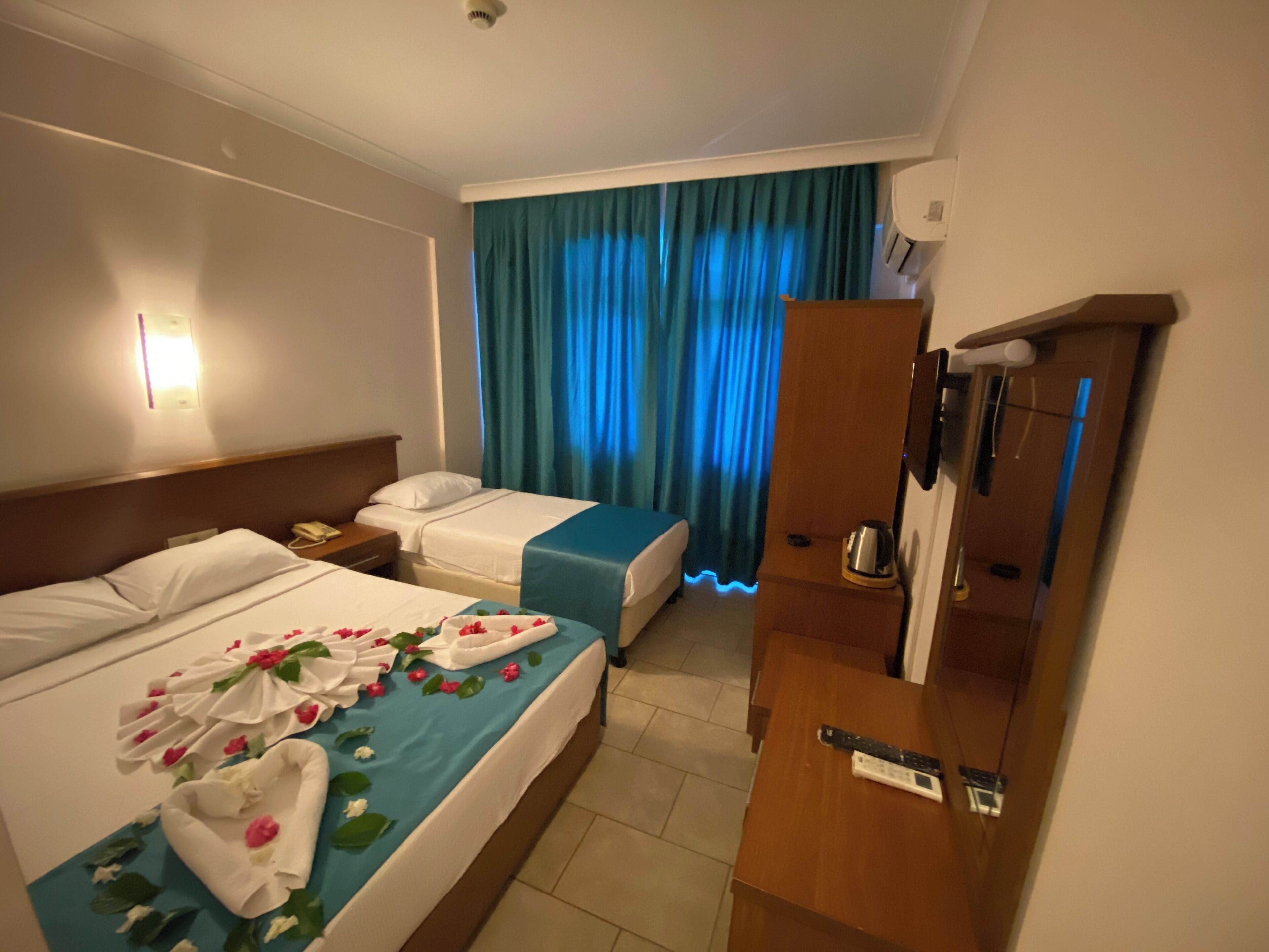Hotellihuone, jossa on kaksi sänkyä, puinen vaatekaappi, työpöytä ja kylpyhuone, jossa on suihku.