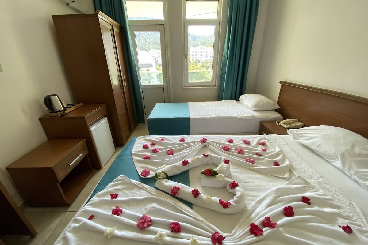 Une chambre d’hôtel avec deux lits, un bureau, une armoire et une vue sur la verdure par les fenêtres.