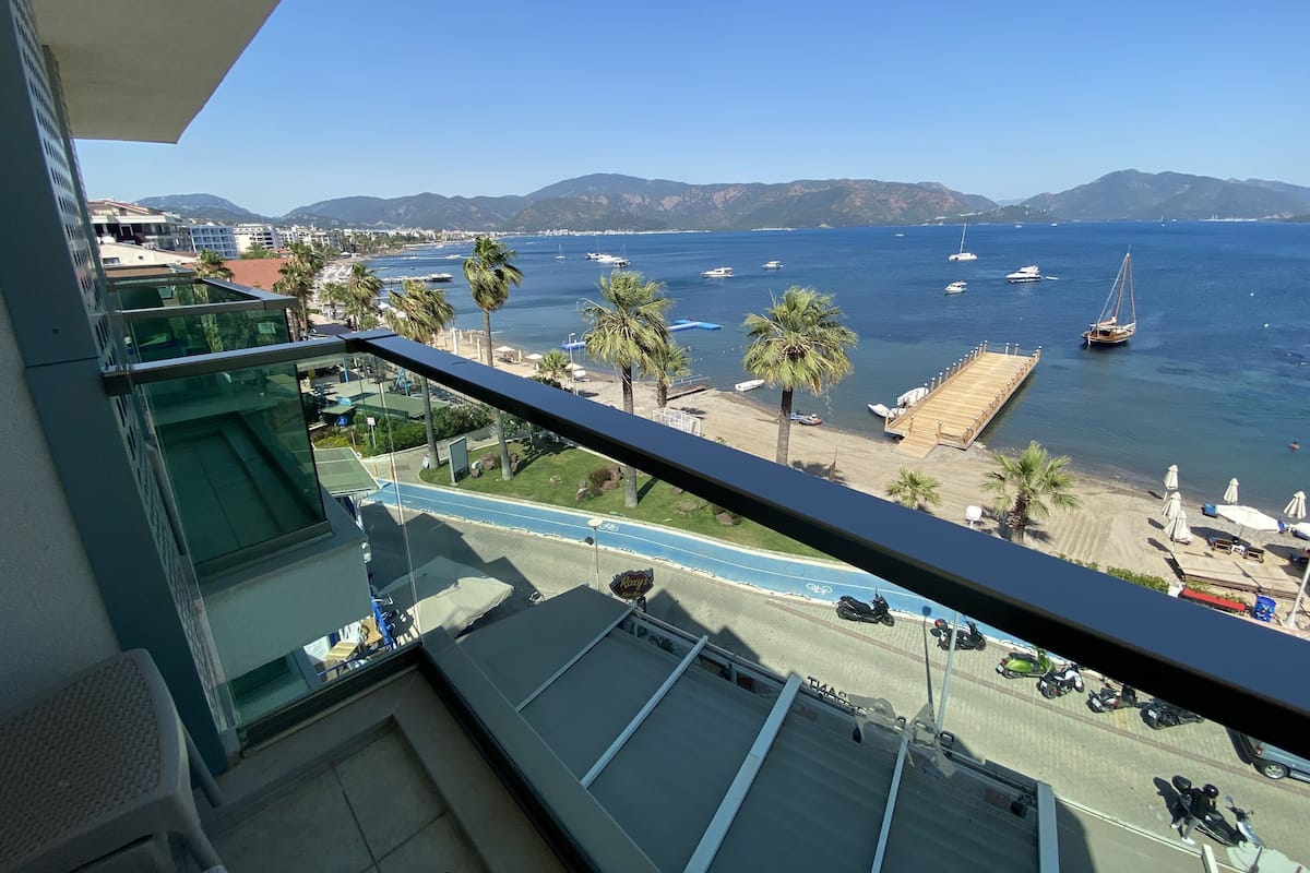 Un balcon avec vue sur une plage, des palmiers et des bateaux sur l’eau.