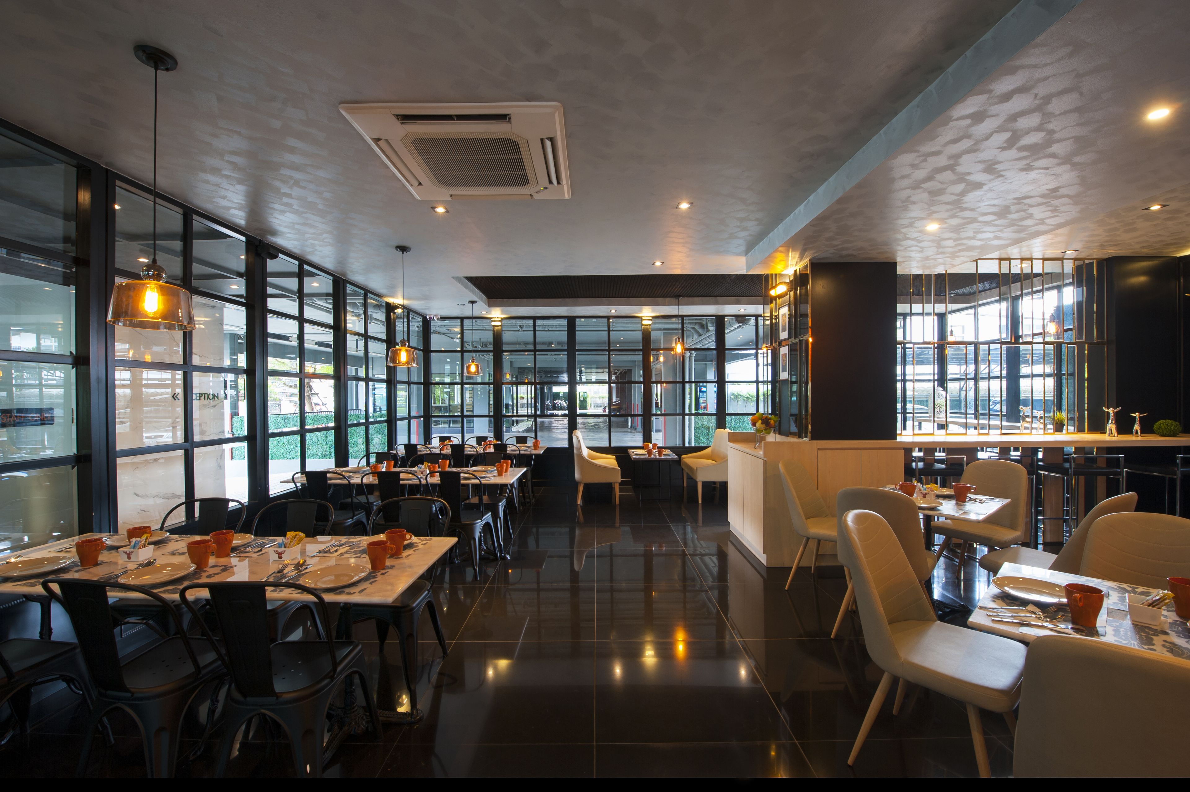 Een modern restaurant met hoge plafonds, grote ramen en een mix van zwarte en witte stoelen.