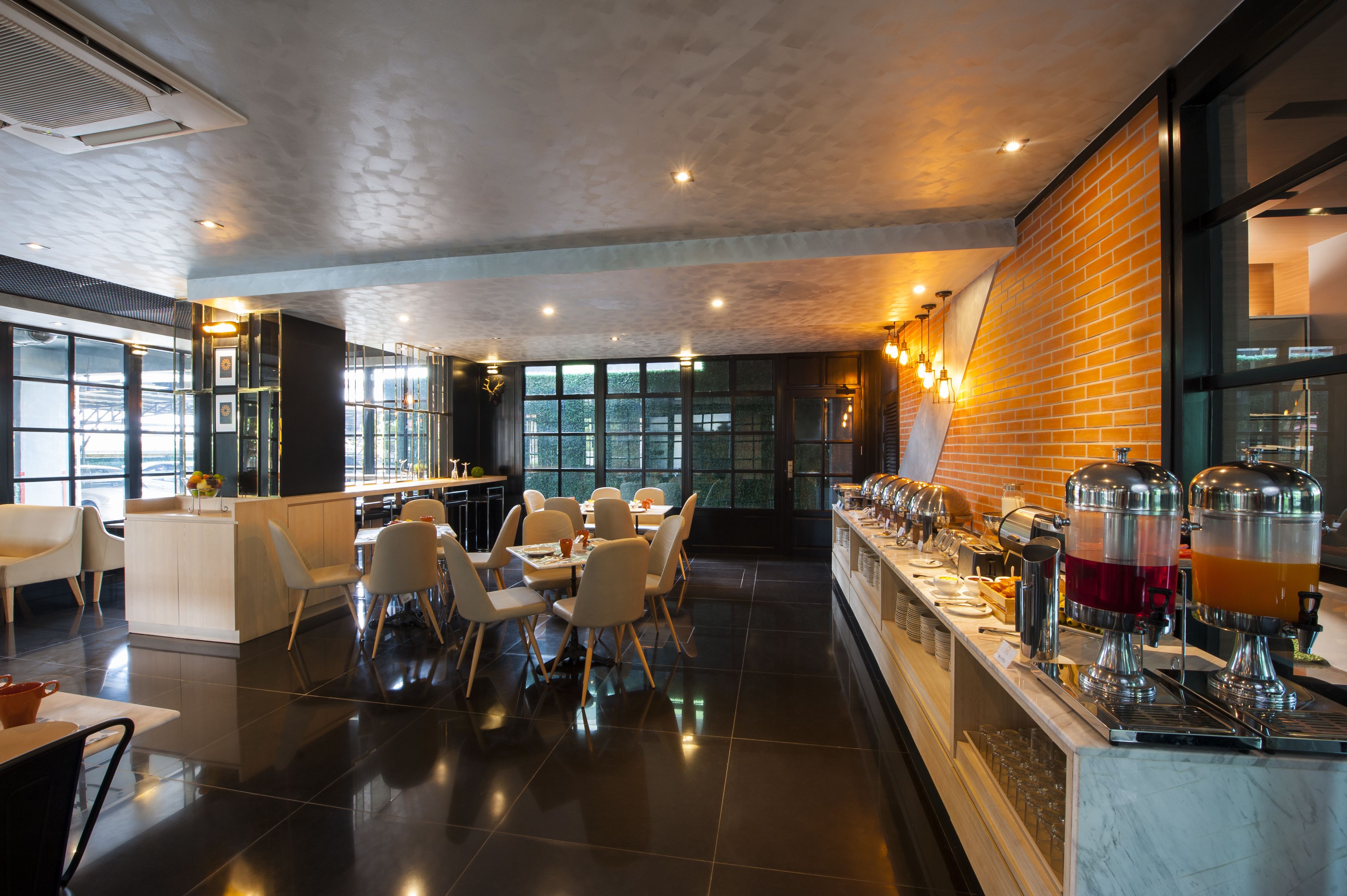 Een modern restaurant met een bakstenen muur, een buffetgedeelte met drankdispensers, en een zithoek met tafels en stoelen.