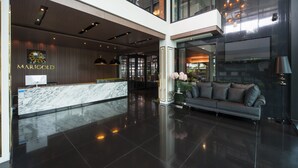 A modern lobby with a marble reception desk, a sofa, and a large window. - Marigold Sukhumvit (Samut Prakan)