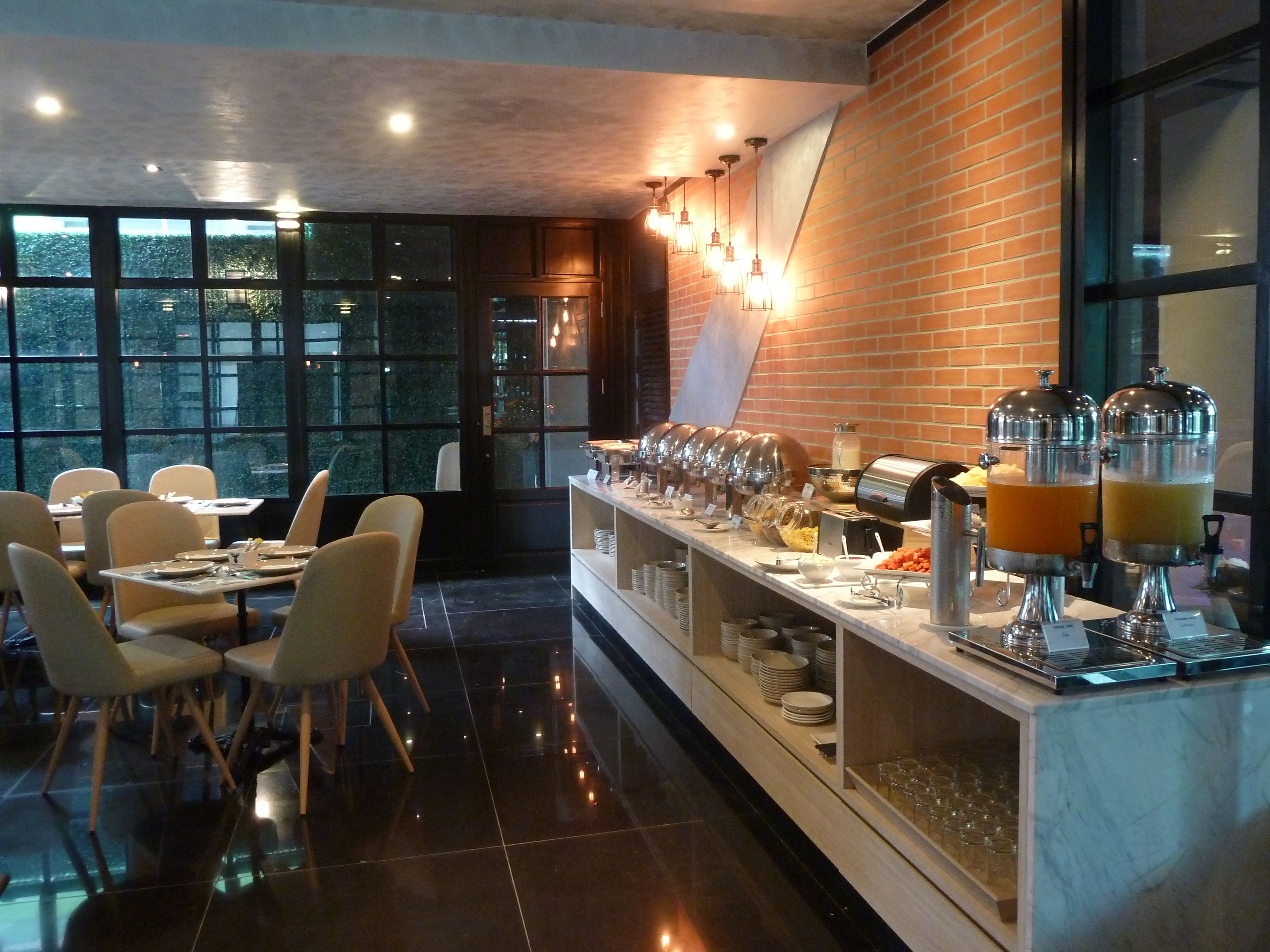 A buffet area with a brick wall, a glass partition, and a variety of food and drink dispensers.