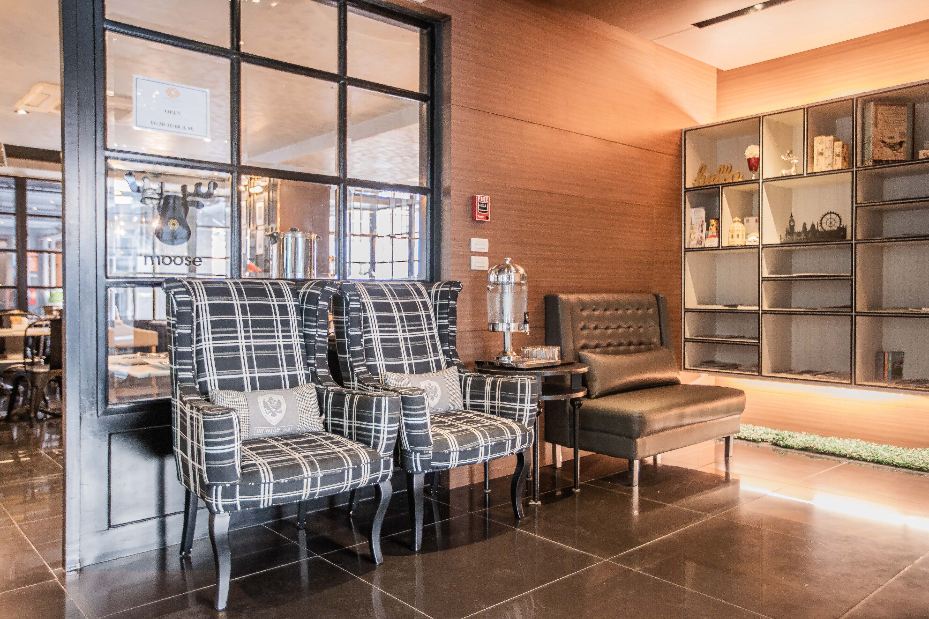 A lobby with a seating area featuring plaid chairs, a leather sofa, and a display of items on shelves.