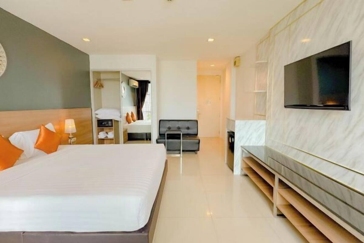 Habitación de hotel moderna con una cama grande, televisor montado en la pared, una zona de estar y un baño visible a través de una puerta abierta.