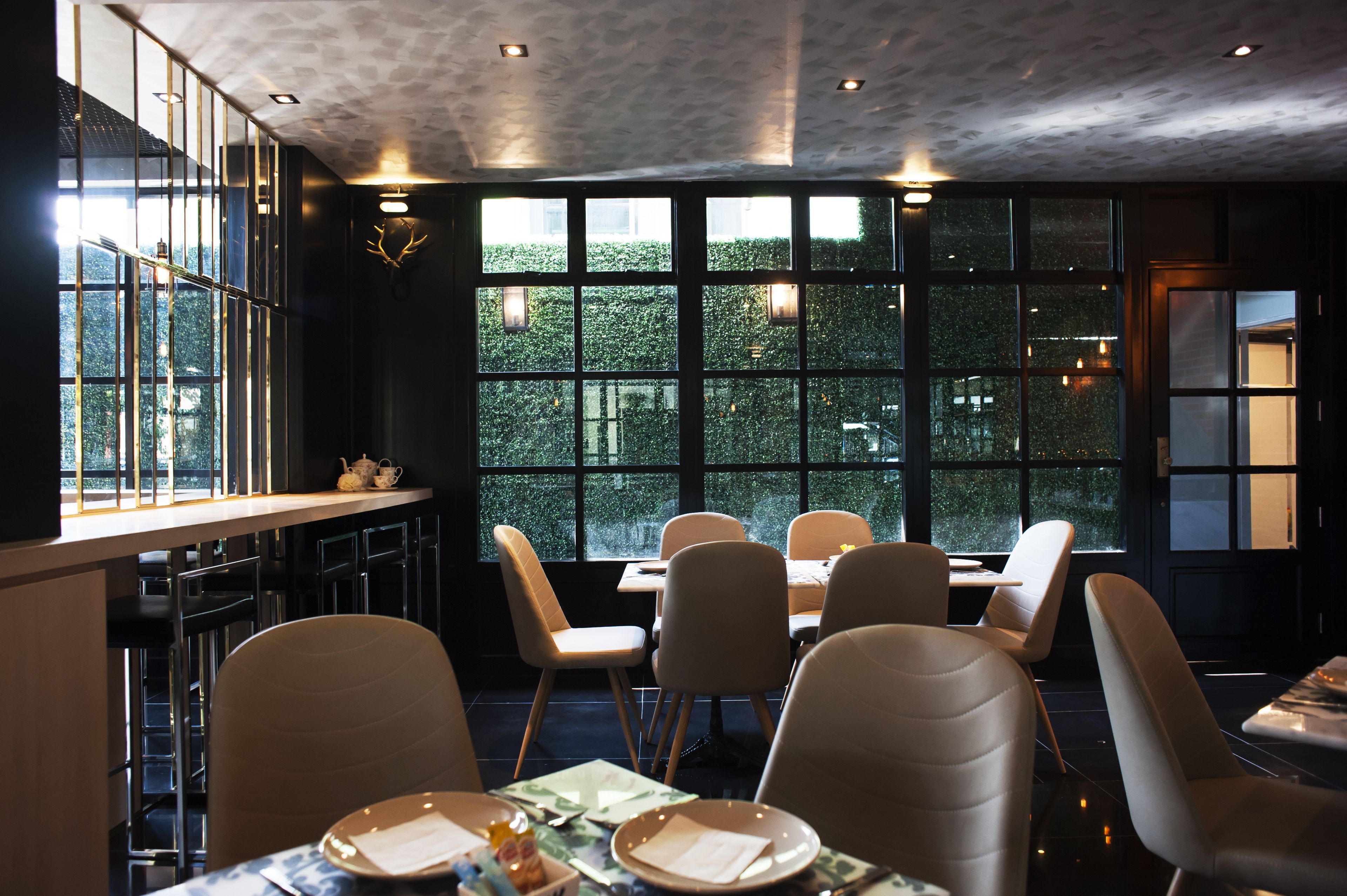 A restaurant with a modern interior, large windows, and a view of greenery outside.