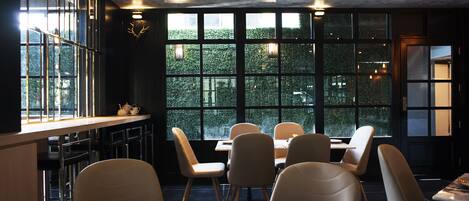 A restaurant with a modern interior, large windows, and a view of greenery outside.