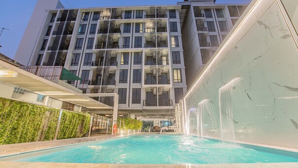 A modern building with a swimming pool, multiple balconies, and a waterfall feature. - Marigold Sukhumvit (Samut Prakan)