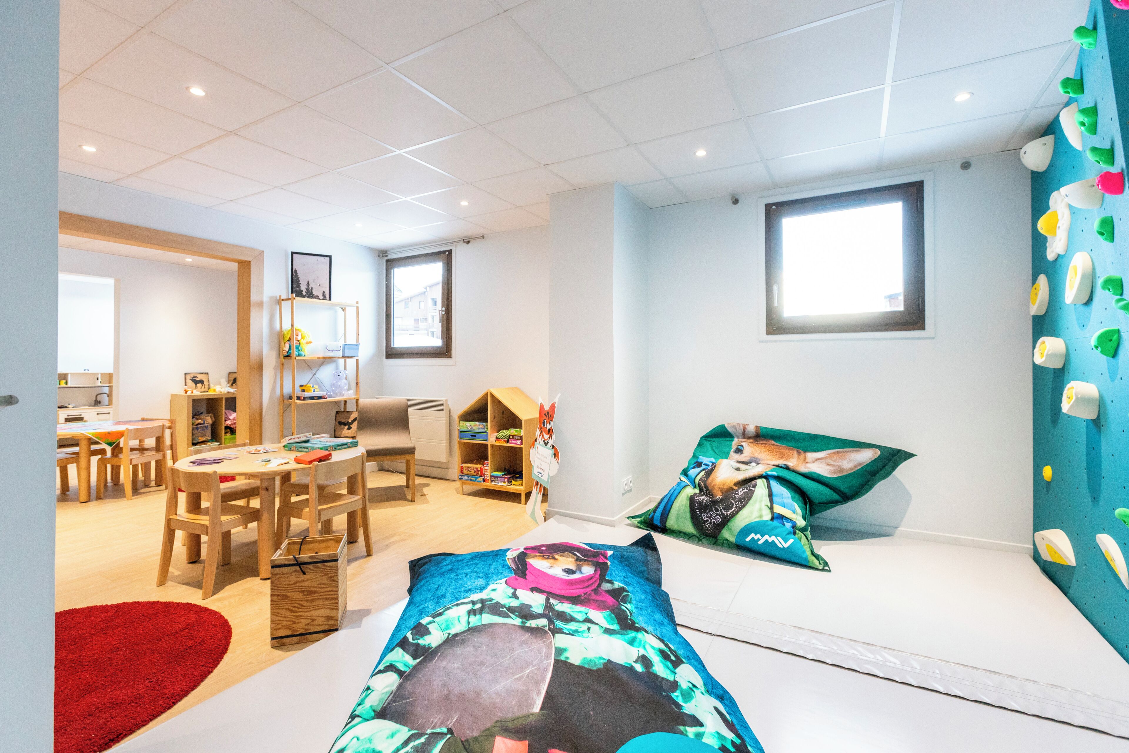 A children's playroom with a climbing wall, a red rug, and a bookshelf.